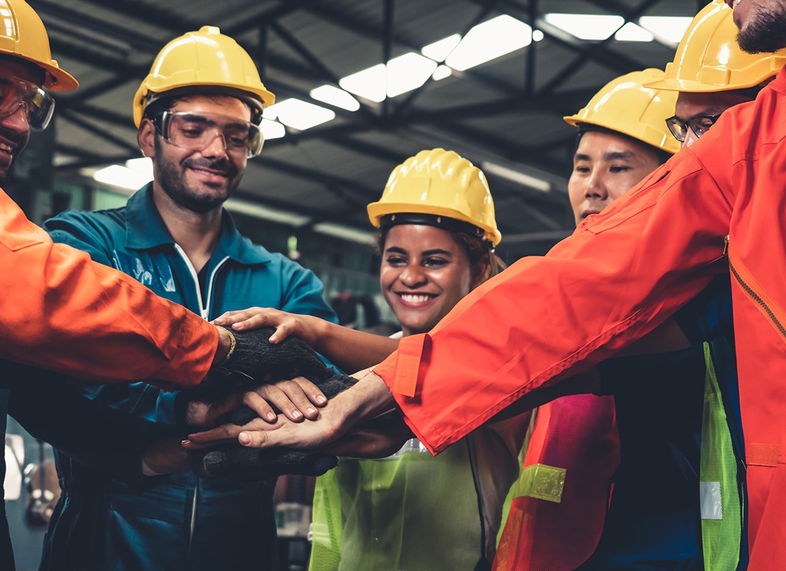 Insurance by Industry - Cheerful Group of Employees Working Inside a Manufacturing Facility Celebrating Success by Putting Their Hands Together
