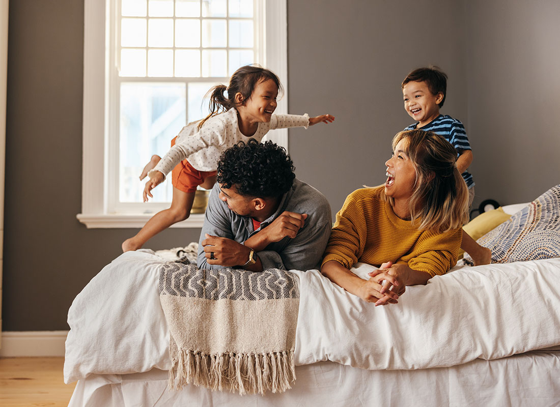 Personal Insurance - View of Parents Laying in Bed Having Fun Playing with Their Son and Daughter at Home